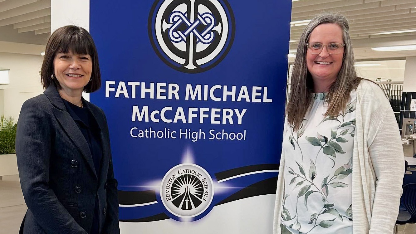 Lynnette Anderson and Heather Kaup in front of a banner at Father Michael McCaffery High School
